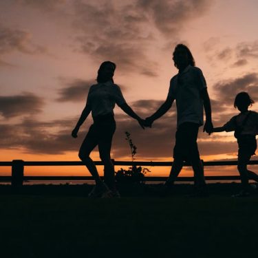 A family walks hand in hand against a vibrant sunset, evoking togetherness and peace.